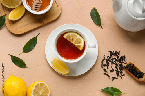Cup of black tea with lemon and leaves on beige background