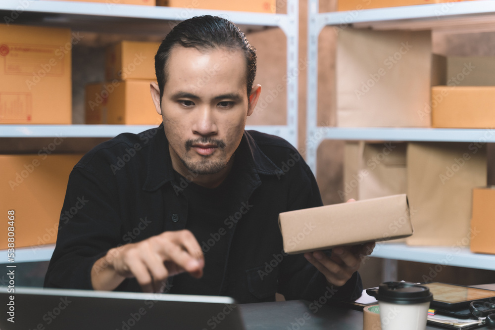 Fototapeta premium man watching and checking the online order for shipping the parcel to customer drinking a coffee. man working with new business about online shopping in home office and small store.