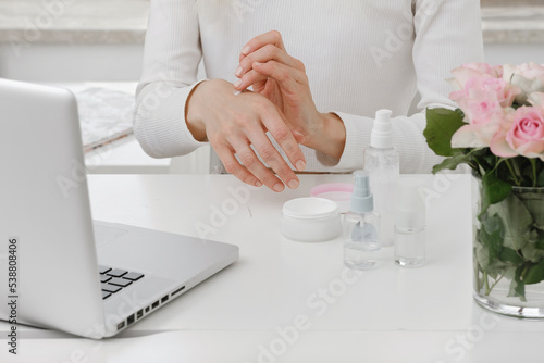 Cream in beauty blogger hands near laptop. Woman make online video content, live broadcast review on cosmetic products. Cosmetology course, skin care tutorial. Close-up