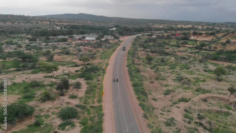 Drone takes an clockwise rotating shot of the two biker driving in the highway of Tharparkar in Sindh. Drone takes an clockwise rotating shot of the two biker driving in the highway of Tharparkar in Sindh.