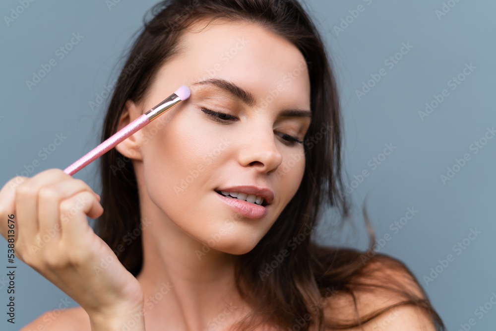 Close-up beauty portrait of woman with perfect skin and natural makeup, full nude lips, holding a bright pink eyeshadow brush, cosmetic concept Close-up beauty portrait of woman with perfect skin and natural makeup, full nude lips, holding a bright pink eyeshadow brush, cosmetic concept