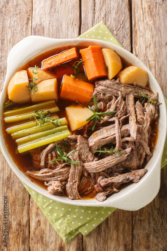 Homemade Slow Cooker Pot Roast with Carrots, Celery and Potatoes closeup in the bowl on the wooden table. Vertical top view from above photo