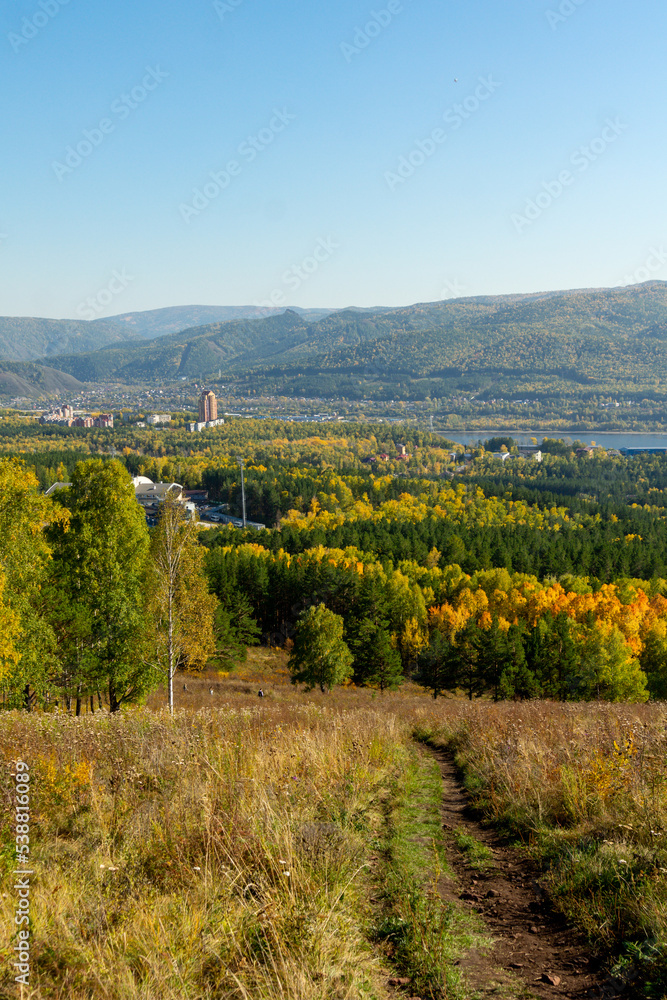 Autumn landscape. A path through an autumn meadow. View of the city, river and hills.