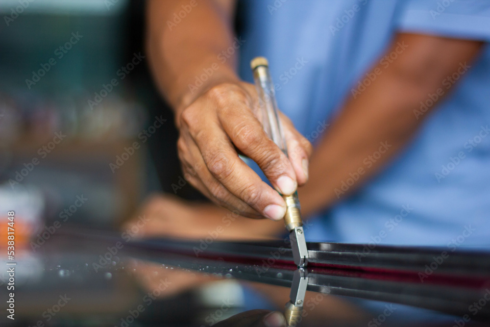 Fototapeta premium Glass technician uses carbide wheel oil-filled glass cutter, a special type to cut glass for customers.