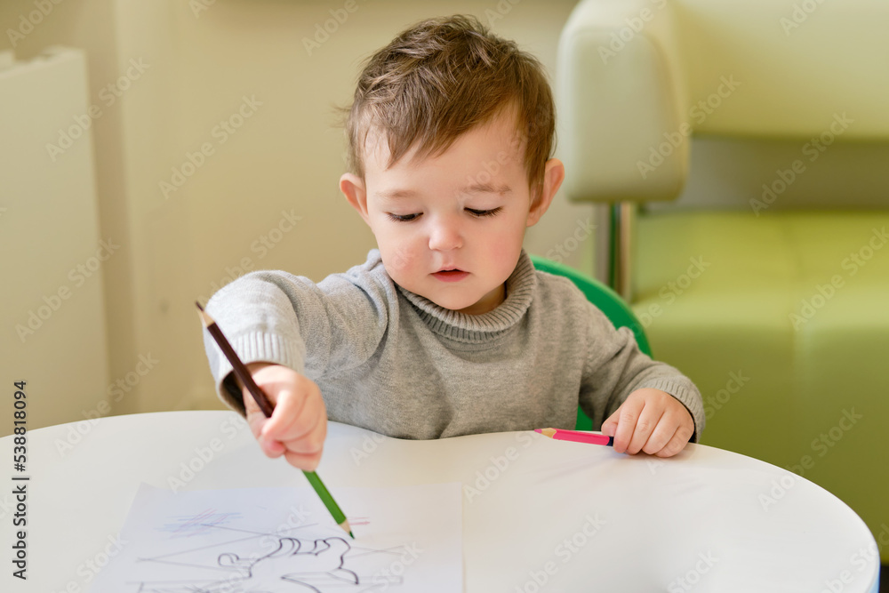 Toddler baby learns to draw with a pencil on a white sheet of paper. Child boy learning to color coloring book. Kid aged one year and three months Toddler baby learns to draw with a pencil on a white sheet of paper. Child boy learning to color coloring book. Kid aged one year and three months