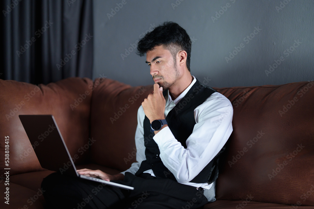 Portrait of a handsome, discreet Asian man sitting on the sofa using a computer Portrait of a handsome, discreet Asian man sitting on the sofa using a computer