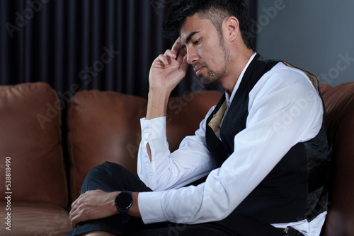 A portrait of a handsome Asian man sitting on the sofa with a thoughtful expression © Jirapong