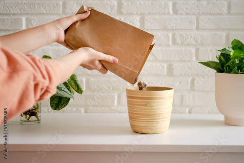 A woman florist pours drainage for planting plants in a flower pot. Preparation for planting a houseplant, white brick wall background