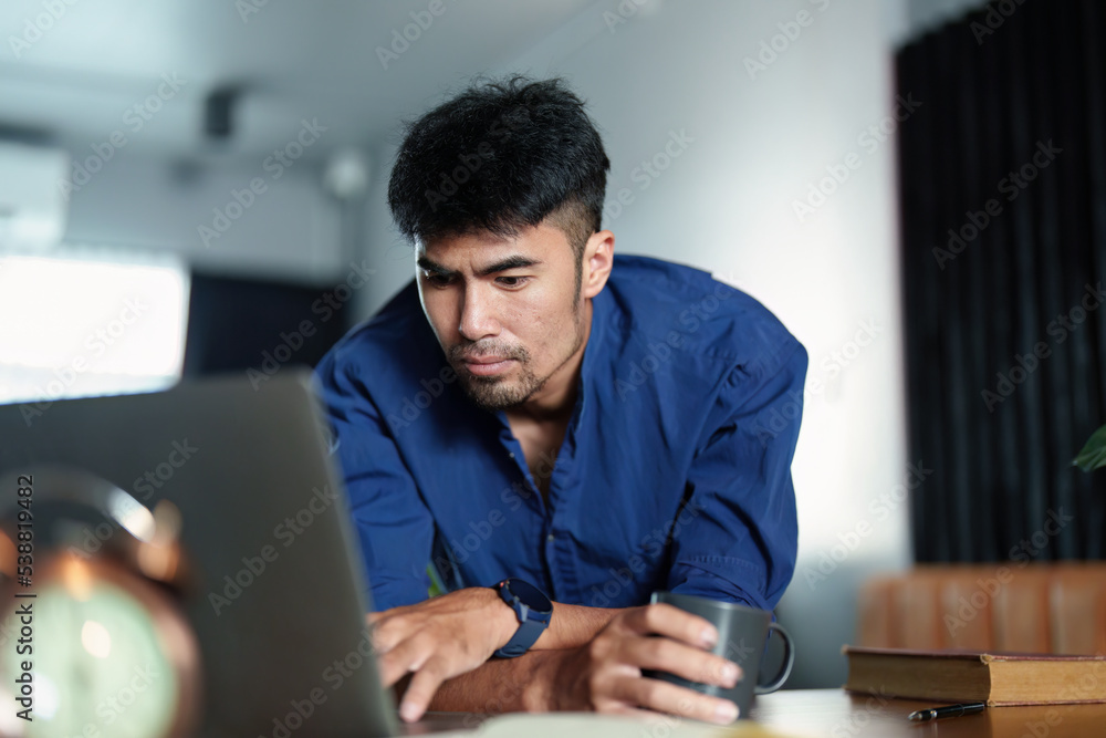 Portrait of an Asian man working on a computer and drinking coffee Portrait of an Asian man working on a computer and drinking coffee