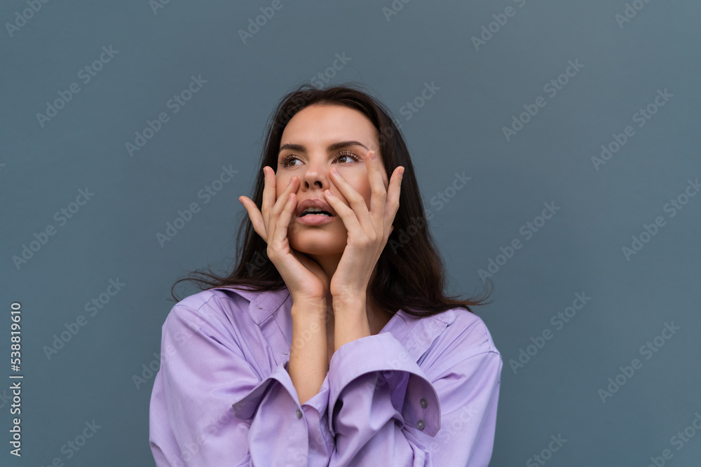 Pretty stylish woman in purple shirt posing on blue wall background, long dark beautiful hair, natural makeup, soft skin Pretty stylish woman in purple shirt posing on blue wall background, long dark beautiful hair, natural makeup, soft skin