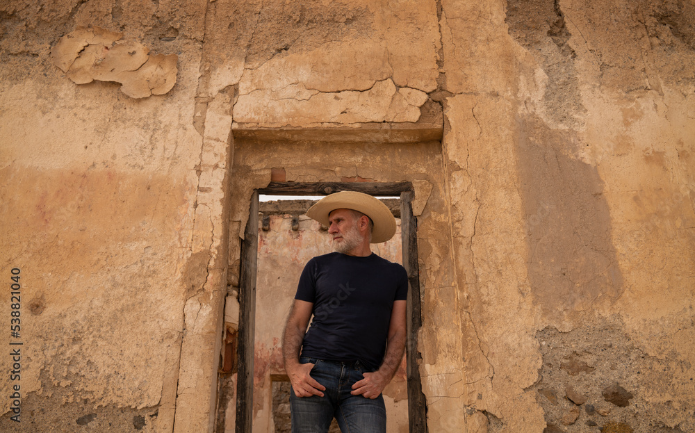Adult man in cowboy hat standing on doorway of abandoned building Adult man in cowboy hat standing on doorway of abandoned building