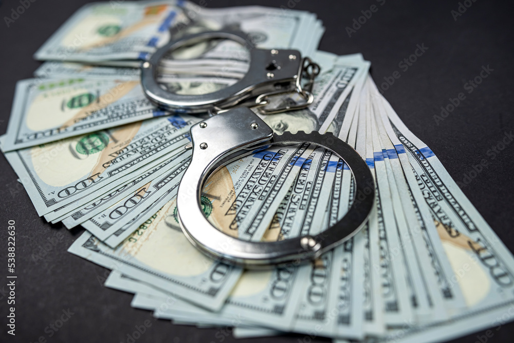 Police handcuffs lie on many dollar bills isolated on black background. Police handcuffs lie on many dollar bills isolated on black background.