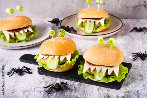 Homemade monster burgers with eyes and tongue for halloween menu on slate and spiders on the table photo