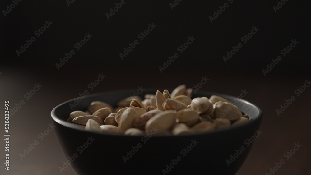 roasted pistachios in black bowl on walnut table roasted pistachios in black bowl on walnut table