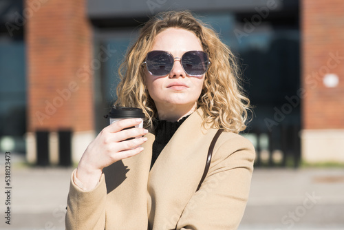 A young Caucasian girl in a coat drinks coffee and thinks while walking in the city in autumn. © Павел Костенко