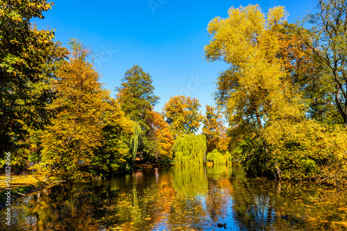 Fototapeta Naklejka Na Ścianę i Meble -  City park and lake with colorful fall trees leaf mosaic in historic old town quarter of Andrychow with Beskidy Mountains in background in Lesser Poland