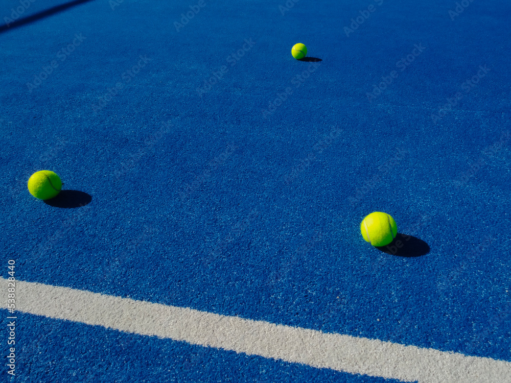 THREE BALLS ON A BLUE PADDLE TENNIS COURT SURFACE
