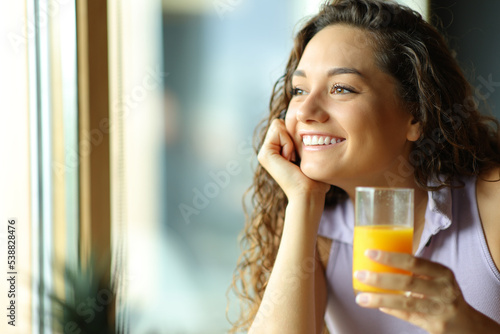 Happy woman holding orange juice looking through window