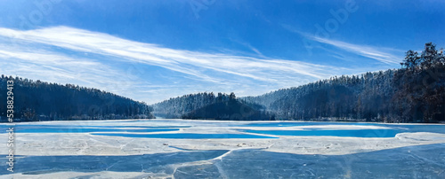 blue ice and cracks on the surface of the ice  frozen lake  forest on background