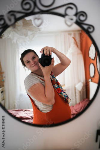 Schilderij op canvas Pregnant woman in overalls takes pictures of herself in mirror on camera