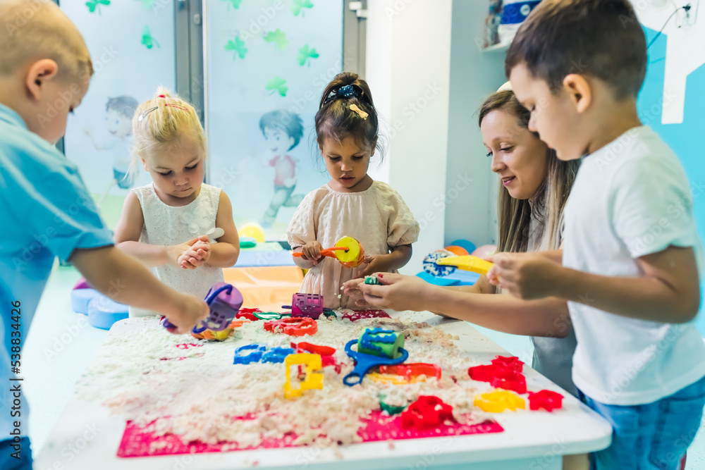 come on, children, let's make funny things - a teacher and her beloved kids playing with kinetic sand, creativity game concept. High quality photo
