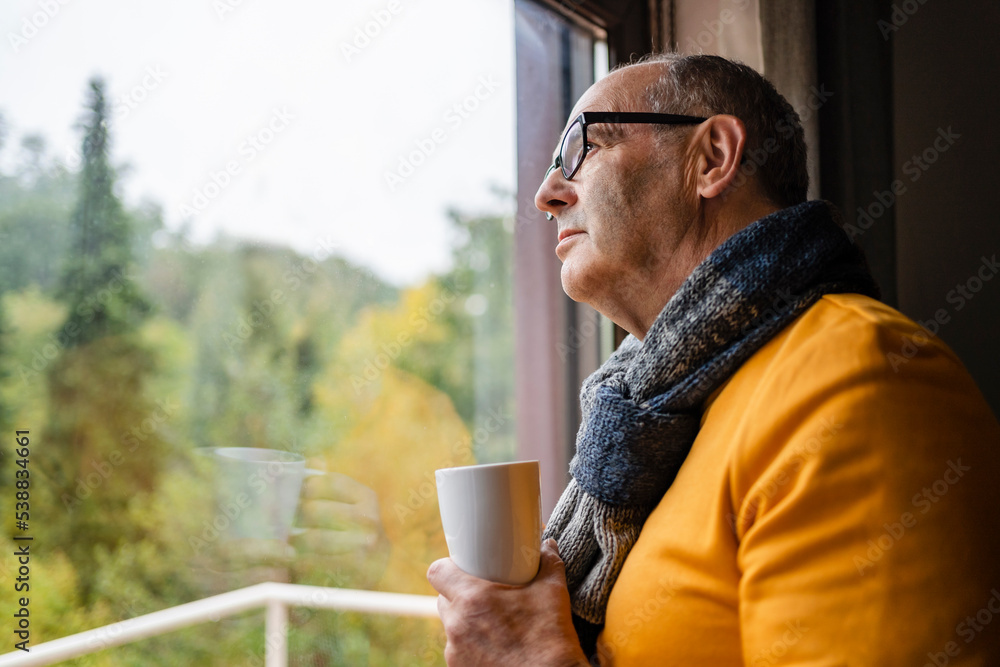 Man looking out of window holding mug at home Man looking out of window holding mug at home