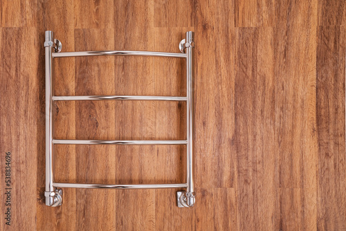 Modern heated towel rail on a wooden wall. Space for text