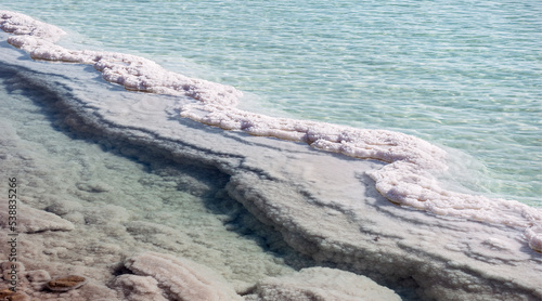 S-shaped salt formation snakes through an evaporation pond in the industrial area of the Dead Sea Yam Hamelah in Israel with clear aquamarine water in the background photo
