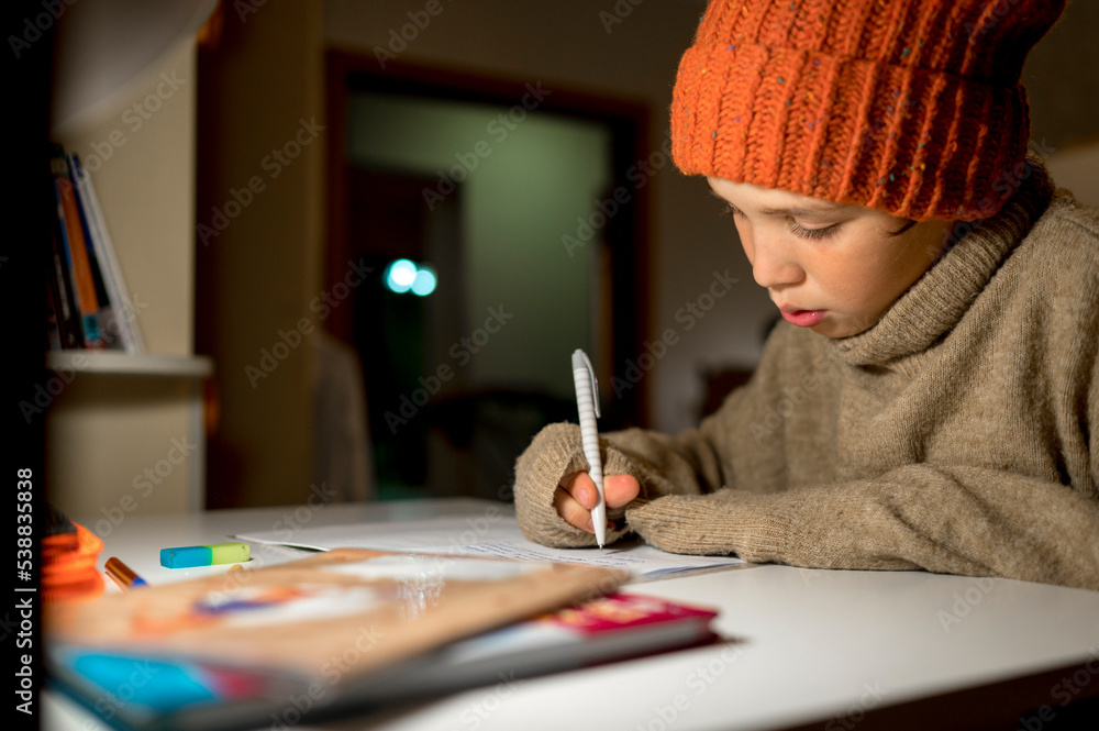 Boy wearing warm clothing studying at table in apartment Boy wearing warm clothing studying at table in apartment