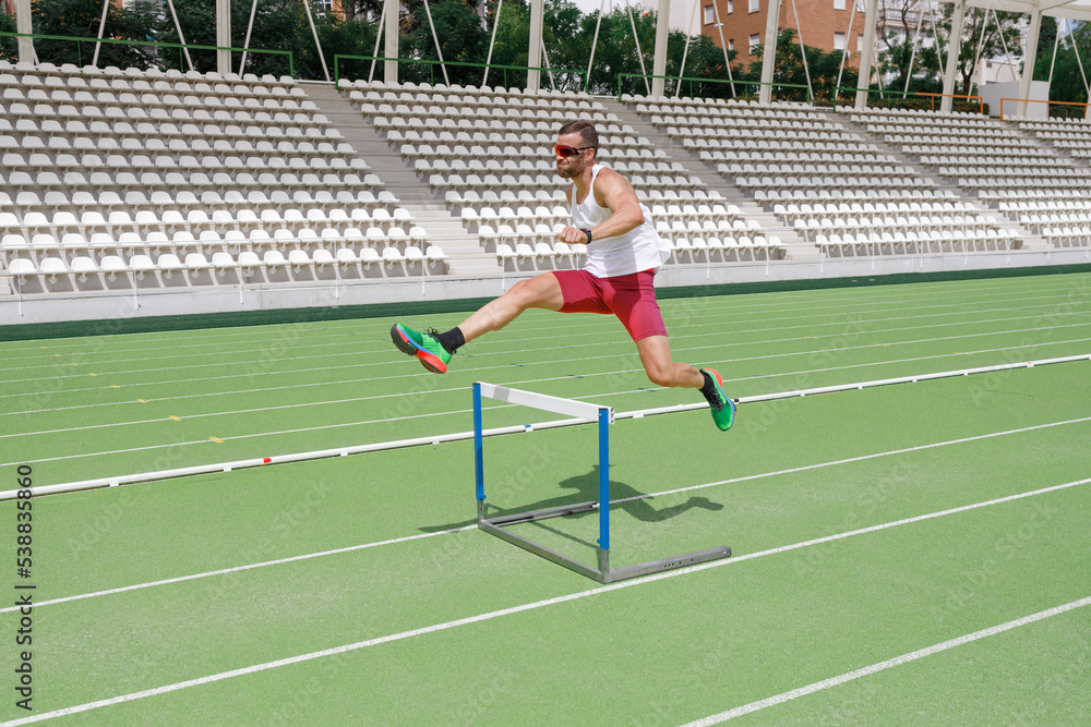 Athlete jumping over hurdle on sports track Athlete jumping over hurdle on sports track