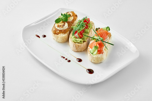 Set of bruschetta with salmon, avocado and goat cheese in a white plate on a white background. Close-up, selective focus.