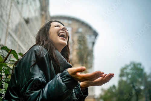 Cheerful woman in raincoat enjoying rain photo
