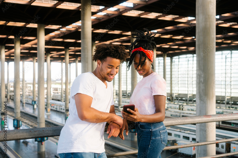 Young woman with bandana sharing smart phone with friend by railing Young woman with bandana sharing smart phone with friend by railing