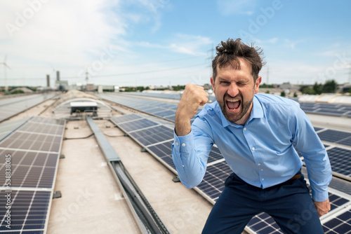 Businessman with mouth open gesturing fist in front of solar panels photo