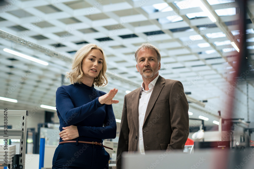 Blond businesswoman gesturing and discussing with colleague at industry Blond businesswoman gesturing and discussing with colleague at industry