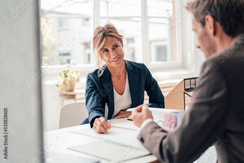 Businesswoman discussing with client reading agreement at office