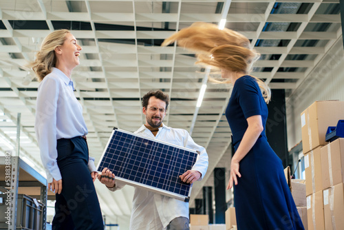 Carefree businessman playing with solar panel by colleagues at warehouse