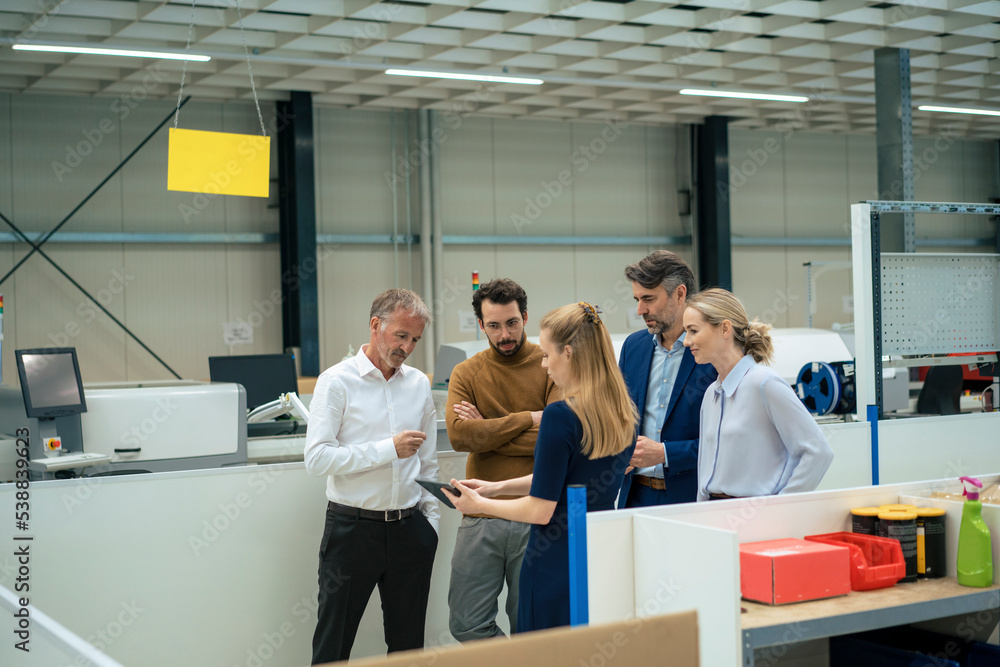 Businesswoman discussing with colleagues over tablet PC in industry Businesswoman discussing with colleagues over tablet PC in industry