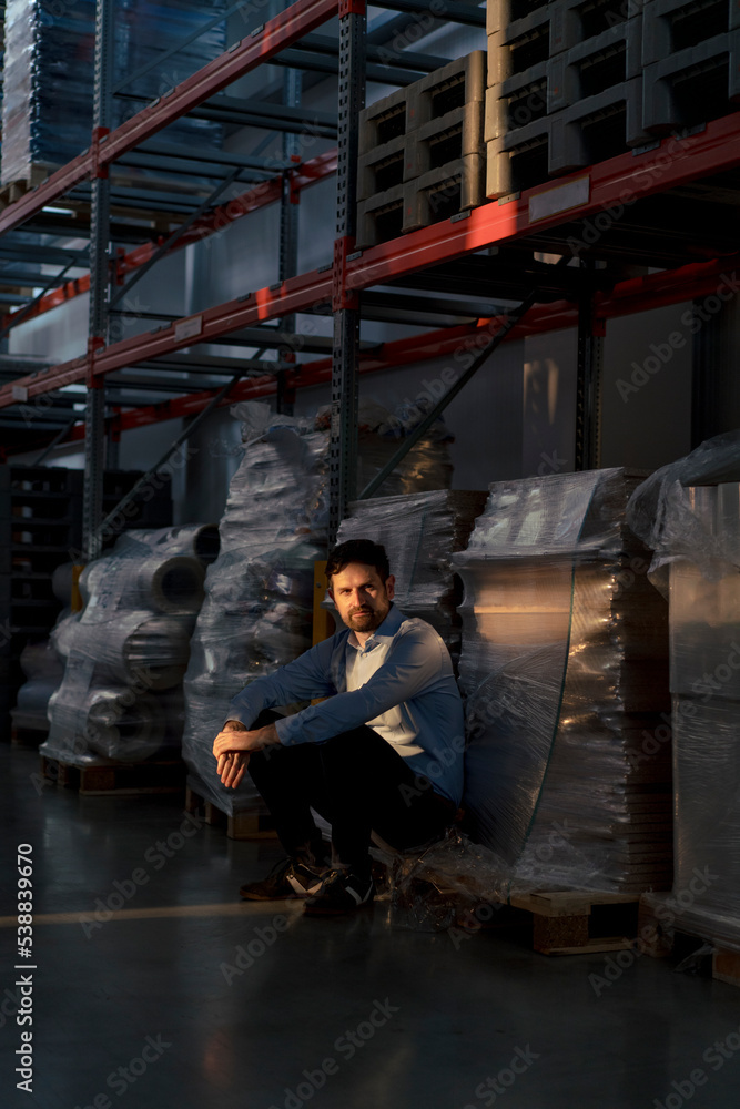 Businessman crouching by rack in warehouse Businessman crouching by rack in warehouse