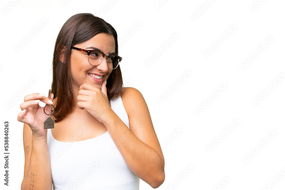 Young caucasian woman holding home keys isolated on green chroma background thinking an idea and looking side Young caucasian woman holding home keys isolated on green chroma background thinking an idea and looking side