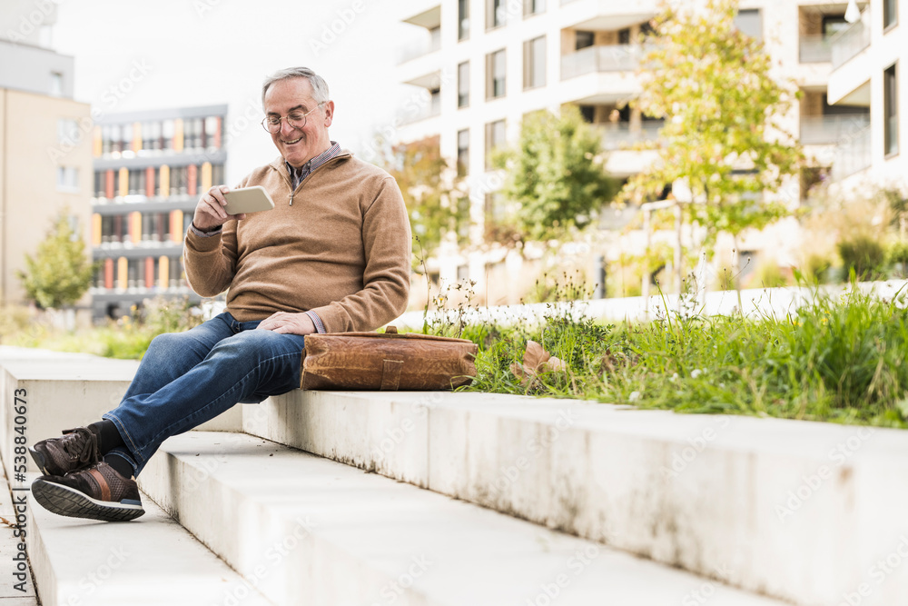 Happy senior man using smart phone sitting on staircase Happy senior man using smart phone sitting on staircase