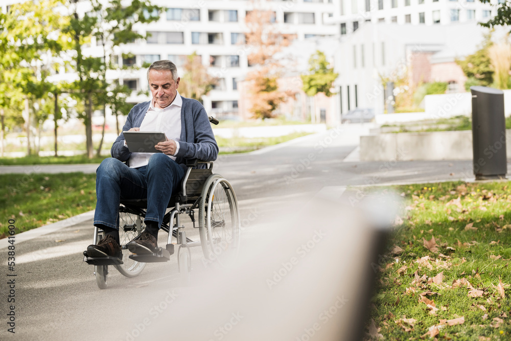 Senior man using tablet PC sitting on wheelchair Senior man using tablet PC sitting on wheelchair