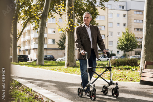 Smiling senior man walking with mobility walker on footpath photo