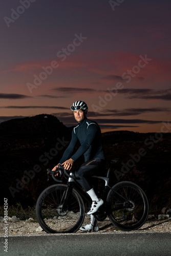 Cyclist wearing protective gear with cycle near roadside at dusk photo