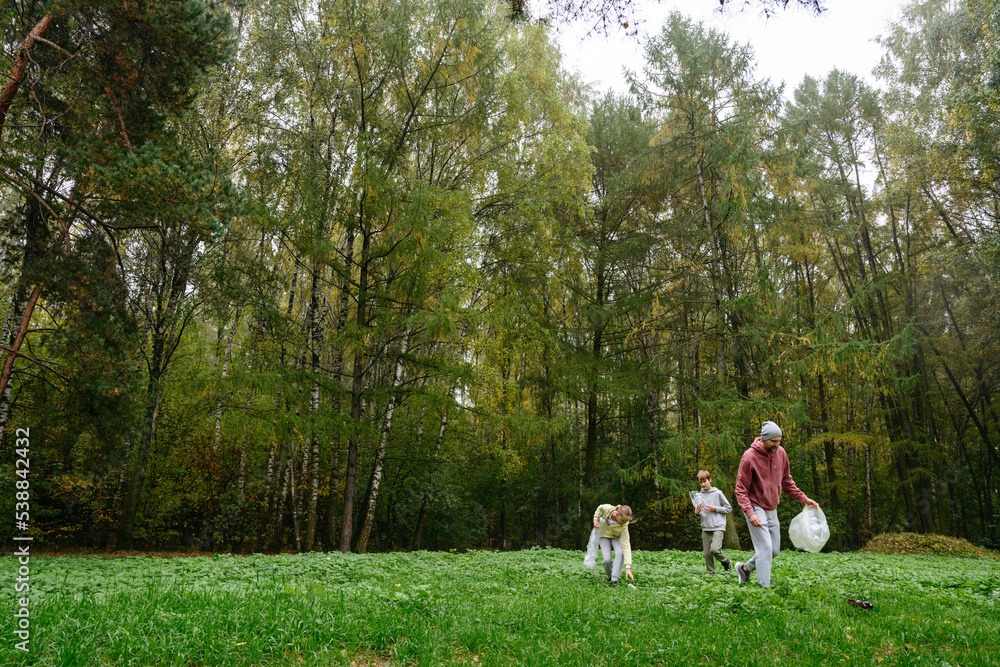Father with son and daughter collecting garbage from grass Father with son and daughter collecting garbage from grass