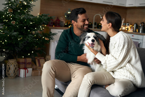 Happy couple with dog sitting at sofa in Christmas © gpointstudio