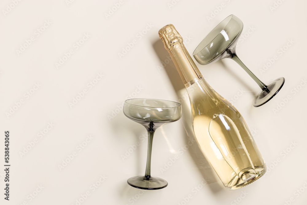 Champagne or sparkling wine bottle, champagne glasses from tinted grey glass on beige background. Festive drink minimal concept. Modern wine glasses, dark colored glass. Creative top view, flat lay Champagne or sparkling wine bottle, champagne glasses from tinted grey glass on beige background. Festive drink minimal concept. Modern wine glasses, dark colored glass. Creative top view, flat lay