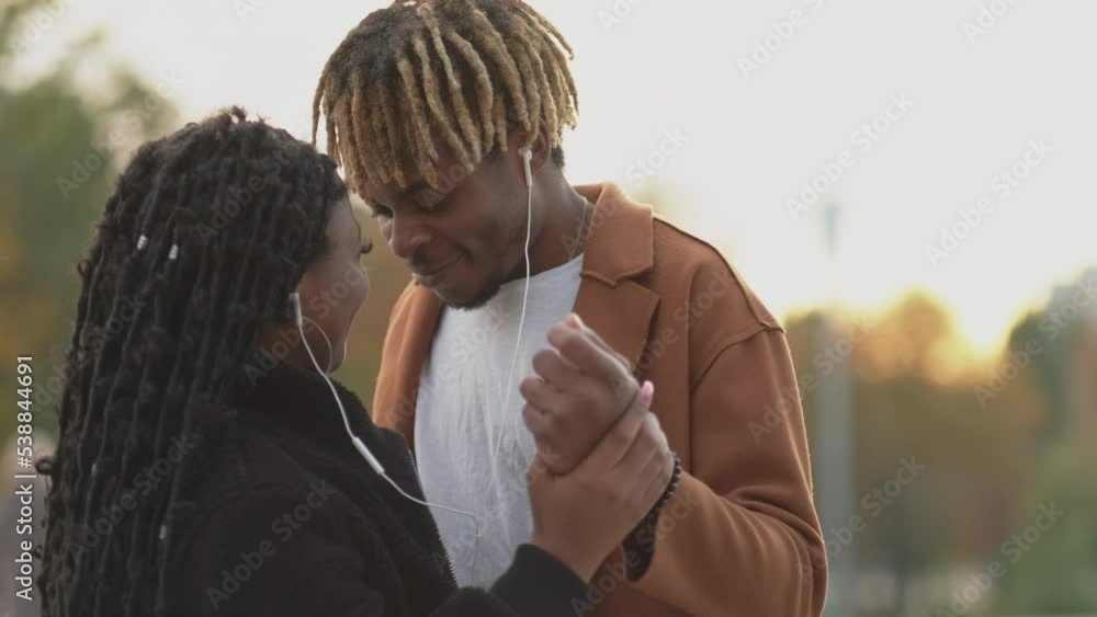 Romantic couple. Enjoying music. Lovely meeting. Happy beloved black woman and man sharing earphones dancing together on street feeling joy.