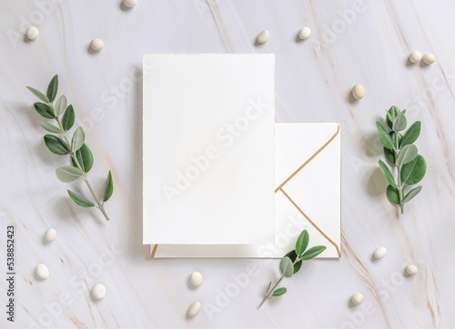 Card and envelope on a marble table near eucalyptus branches and white pebbles, Wedding mockup
