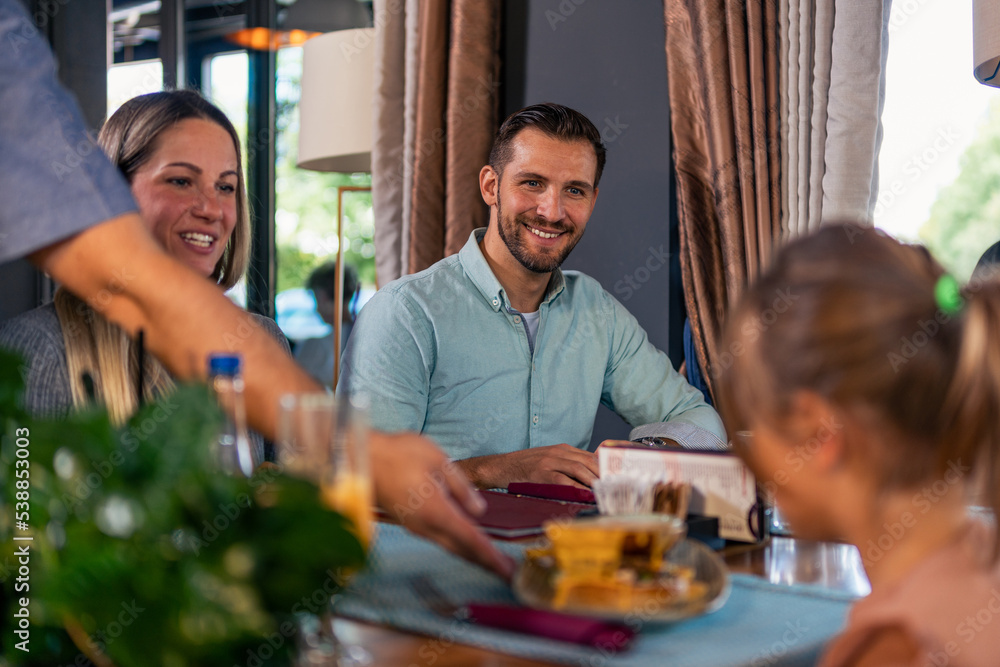 The waiter in the restaurant brings lunch to the whole family of three. Family launch concept. The waiter in the restaurant brings lunch to the whole family of three. Family launch concept.